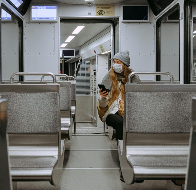 Lady sat on empty train during covid 19 pandemic wearing face mask looking at phone